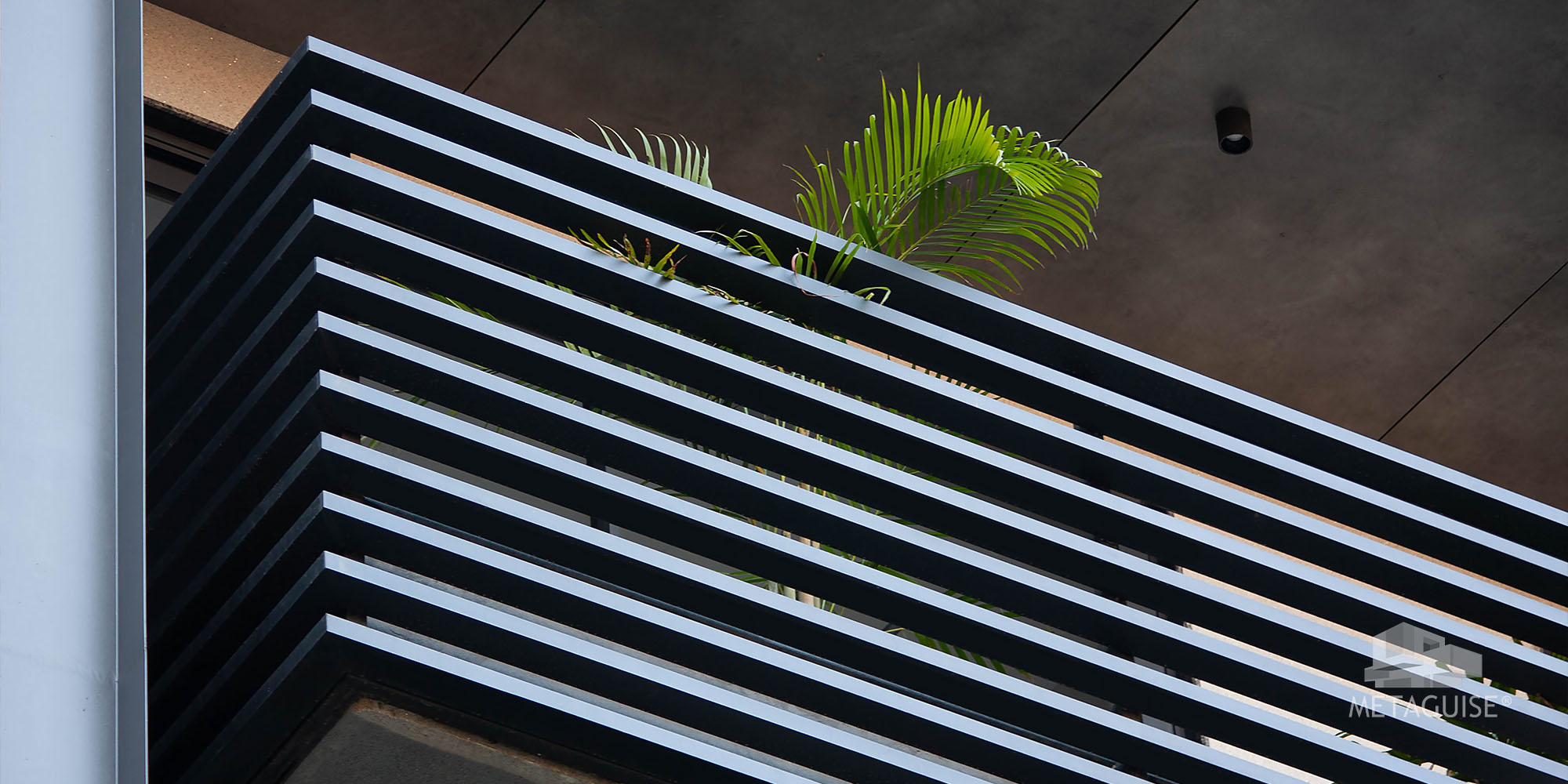 Black horizontal aluminium louvers on a balcony edge with a palm planter above