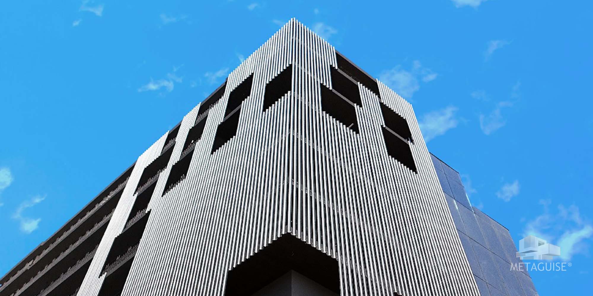 Upward view of a building corner clad in vertical aluminium fins against a blue sky
