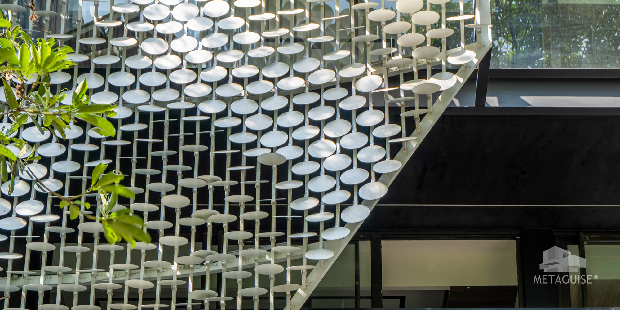 Metaguise circular disc metal cladding on a modern house exterior, seen against dark glazing and green foliage
