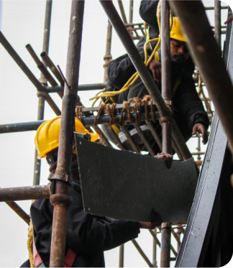 Metaguise installation team assembling facade panel on scaffolding with safety harnesses and yellow helmets.